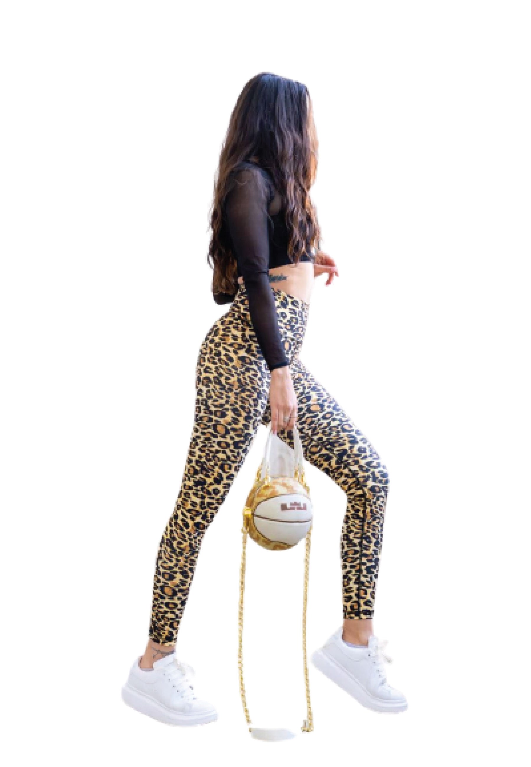 Frau in Lisminas 263 Extra High Waist Leopard Leggings, schwarzem Top, weißen Sneakers, hält eine runde Tasche.
